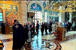 Vernici i sveštenstvo okupljeni u centralnom delu Hrama Preobraženja Gospodnjeg na Zlatiboru tokom dugog bratskog sastanka. Jedan sveštenik vrši čin blagosiljanja ili ispovesti vernika, dok se u pozadini vidi karakteristična mermerna rozeta na podu i bočni oltar sa drvenim elementima i ikonama