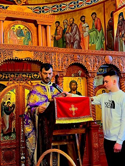 Sedam pravoslavnih sveštenoslužitelja iz zlatiborskog namesništva u sabornom činu čitanja Svetih Jevanđelja tokom Svete tajne jeleosvećenja u hramu Svetog arhangela Gavrila u Čajetini. Slika detaljno prikazuje sveštenike iz Sirogojna i Draglice kako sa strahom Božijim i dubokim pijetetom pripremaju jevanđeljske knjige za početak molitve za zdravlje. Svaki od sedam sveštenika naizmenično čita odeljke koji svedoče o Hristovoj moći isceljenja, dok verni narod Čajetine i Zlatibora u potpunoj tišini sluša reči spasenja. Ovaj molitveni trenutak simbolizuje živu reč Božiju koja se izliva na parohiju čajetinsku, prizivajući blagodat za sve bolesne i nemoćne pred praznik Vaskrsenja 2026. godine